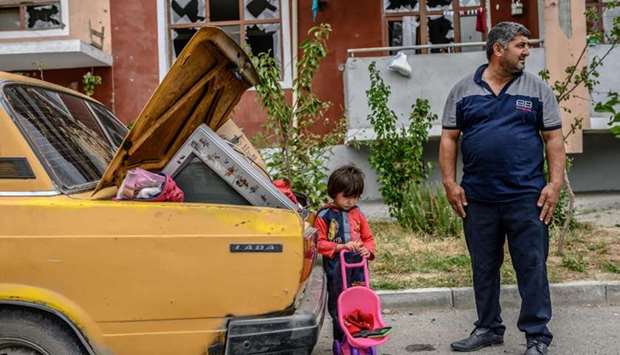 A man stands with his kid by a car outside a damaged apartment building after the family took their last belongings from their flat during a ceasefire during a military conflict between Armenia and Azerbaijan over the breakaway region of Nagorno-Karabakh, in the town of Terter, Azerbaijan