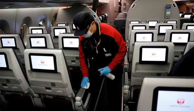 A staff member of Japan Airlines wearing a protective face mask and gloves cleans the cabin of a plane after performing a domestic flight