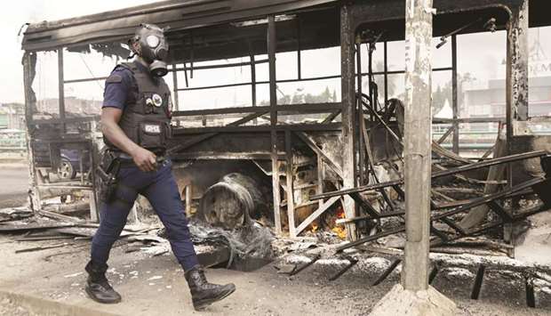A riot police member walks next to a bus which was burned early in the morning by protesters against the Ivorian President Alassane Ouattarau2019s decision to stand for a third term, in Abidjan, yesterday.