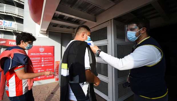 An employee takes the temperature of a soccer fan as he arrives to attend the first Mexican league match in person, since the start of the coronavirus disease outbreak, during a match between Necaxa and Tijuana, at the Victoria stadium, in Aguascalientes, Mexico