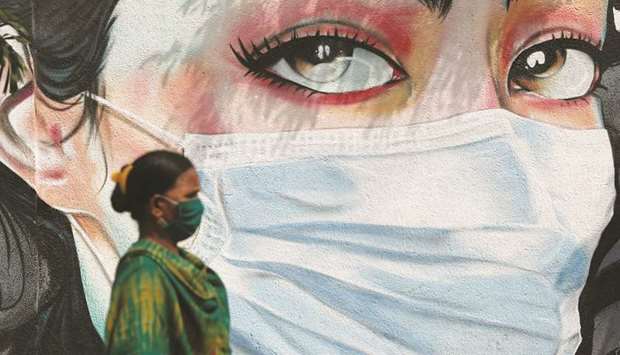 A woman walks past a graffiti of a girl wearing a protective mask amidst the spread of the coronavirus disease in Mumbai.