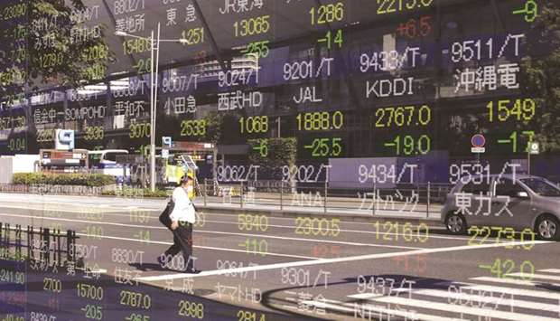 A pedestrian wearing a protective face mask is reflected on an electronic stock board outside a securities firm in Tokyo. The Nikkei 225 closed 0.4% down at 23,331.94 points yesterday.