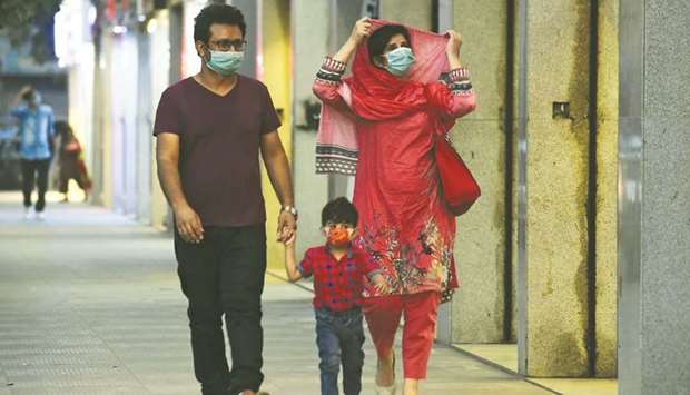 A family wearing facemasks as a preventive measure against the coronavirus walk alongside a street in Karachi yesterday.  (AFP)