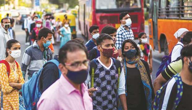 Commuters wearing face masks wait at a bus stand in New Delhi yesterday.