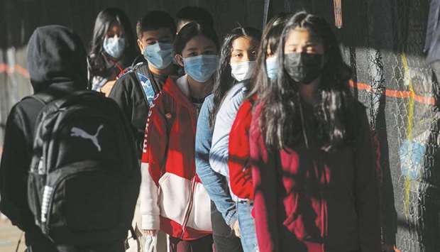 Children wait in line for health screenings before entering a school.