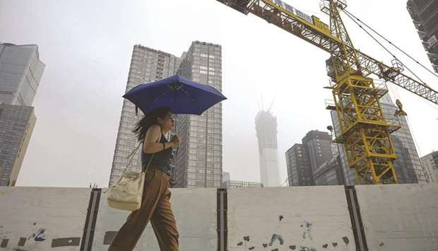 A woman holding an umbrella walks past a construction site in Beijing (file). The $5tn property sector accounts for around a quarter of the Chinese economy by some metrics.