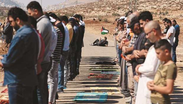 A Palestinian protester waves a national flag, as others perform the Friday prayers during a demonstration against the establishment of Israeli outposts on their lands, in Beit Dajan, east of Nablus in the occupied West Bank, yesterday.