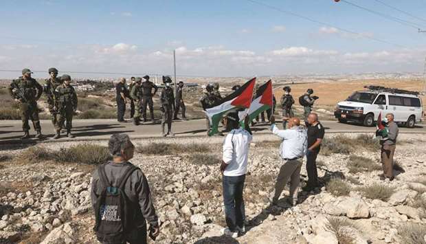 Demonstrators hold Palestinian flags as members of the security forces stand guard during a protest against Israeli settlements in Masafer Yatta, in the occupied West Bank, yesterday.