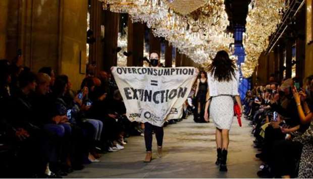 An activist walks on the ramp with a banner that says ,Overconsumption = Extinction, as she crashes the designer Nicolas Ghesquiere Spring/Summer 2022 women's ready-to-wear collection show for fashion house Louis Vuitton during Paris Fashion Week in Paris, France.