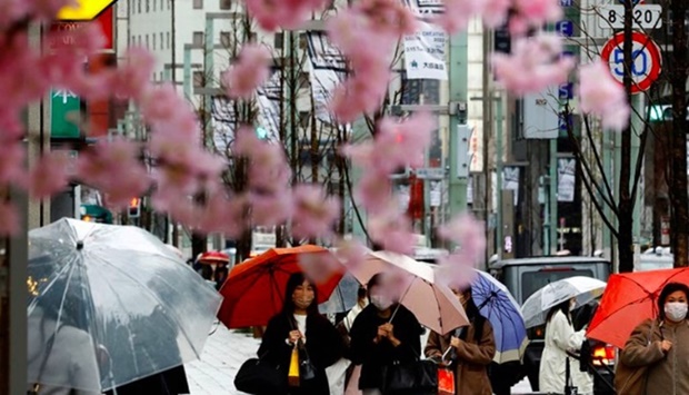 Pedestrians wearing protective face masks, amid the coronavirus disease (Covid-19) pandemic, are seen behind artificial cherry blossom decorations at a shopping district on the first day after the lifting of Covid-19 restrictions imposed on Tokyo and 17 other prefectures, in Tokyo, Japan,