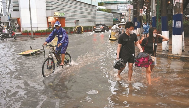 People walk along a flooded street in Manila following heavy rain brought by Tropical Storm Nalgae.