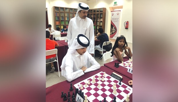 Mohamed al-Mudahka, President of QCF, watches a young participant make a move during the Qatar Center Chess Training Youth Championship.