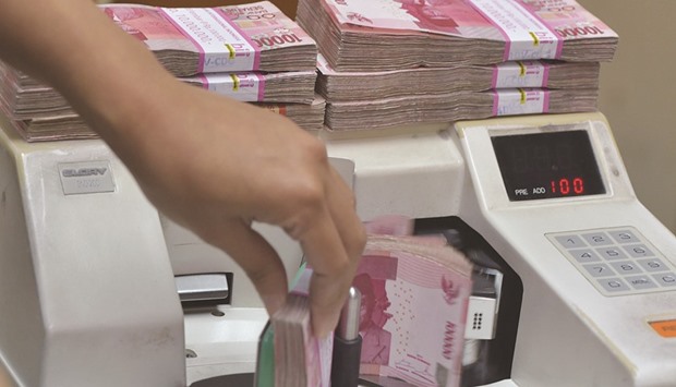 An employee counts rupiah banknotes at a money changeru2019s office in Jakarta. The rupiah plunged to a five-month low yesterday, prompting the nationu2019s central bank to say it stepped in to stabilise the local currency and bond markets.