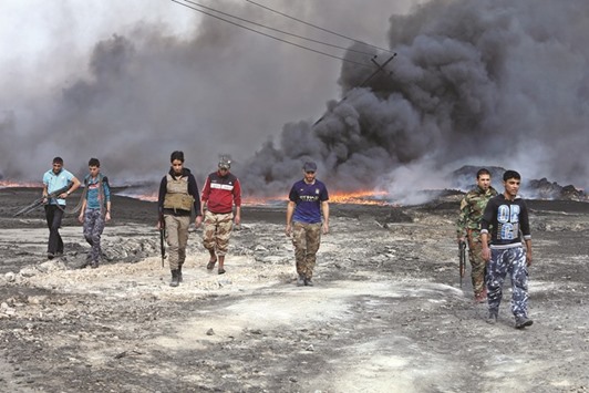 Tribal fighters walk as fire and smoke rises from oil wells, set ablaze by Islamic State militants before they fled the oil-producing region of Qayyara, Iraq, yesterday.