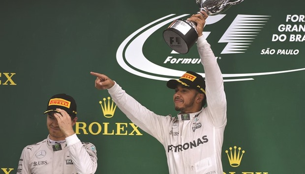 Hamilton celebrates with the trophy after winning the Brazilian Grand Prix ahead of title rival and Mercedes teammate Nico Rosberg (left) yesterday. (AFP)
