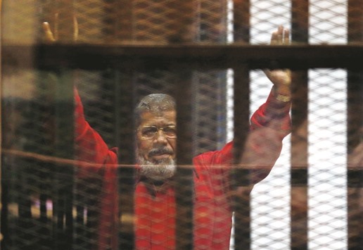 Mohamed Mursi behind bars at a court wearing the red uniform of a prisoner sentenced to death.