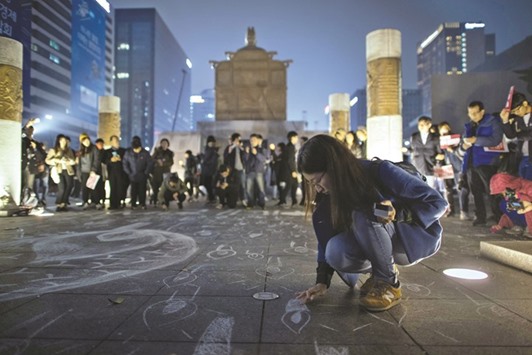A woman uses chalk to draw candles on the pavement last night during the protest in Gwanghwamun square in central Seoul.