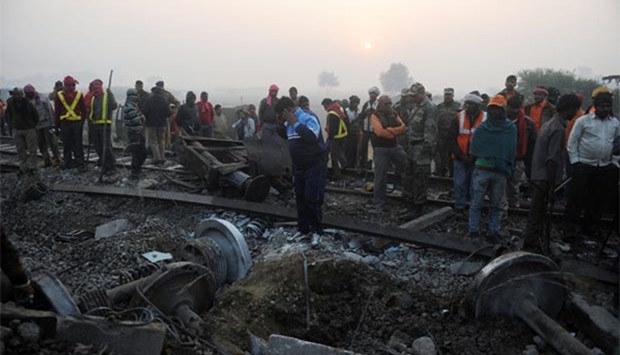 Rescue worker and onlookers stand near the wreckage of the train on the damaged tracks where a train derailed near Pukhrayan in Kanpur district, on Monday.