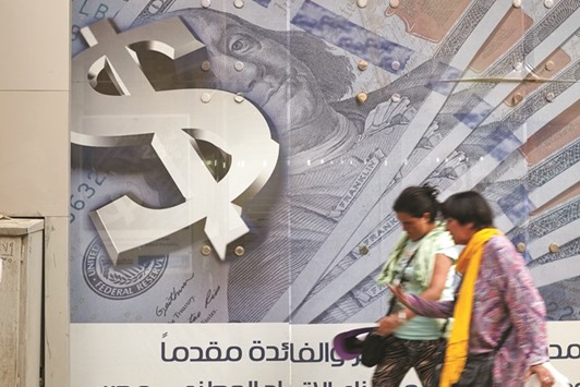 Pedestrians walk past an advertisement displaying a large dollar sign and US dollar banknotes outside a bank in Cairo. Egyptian authorities are trying to reduce the governmentu2019s borrowing costs after abandoning currency controls this month.