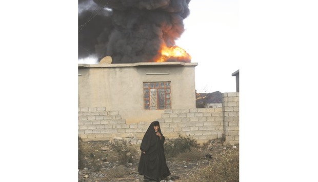 A woman walks as fire and smoke rises from oil wells, set ablaze by Islamic State militants before fleeing the oil-producing region of Qayyara, Iraq, yesterday.