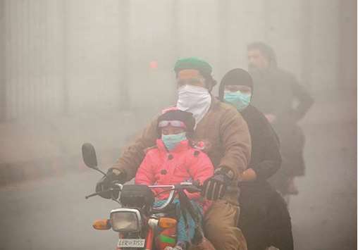People use face masks to protect themselves from morning smog as they ride on bike along a road in Lahore yesterday.