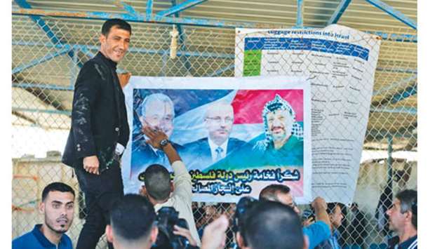 Palestinian men put up a poster displaying President Mahmud Abbas, Prime Minister Rami Hamdallah and late leader Yasser Arafat, at the northern entrance of the Gaza Strip just after the Israeli-controlled Erez crossing, yesterday in Beit Hanun.