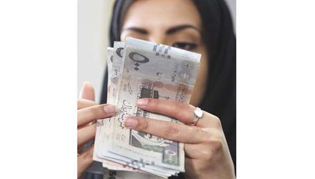 A Saudi woman counts Saudi riyal banknotes at a money exchange shop in Riyadh (file). The kingdomu2019s seven largest banks reported an average drop in loans of around 4.9% at the end of September, compared to the same period of last year.
