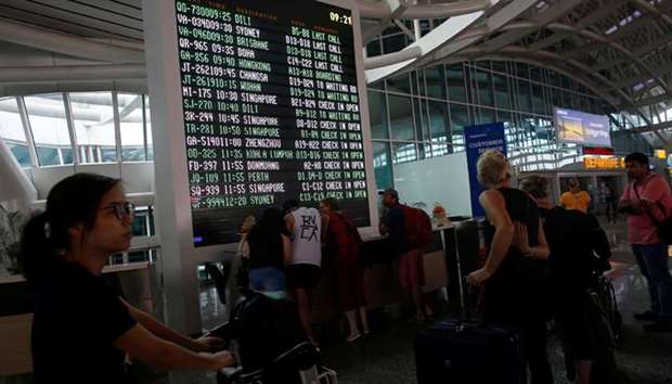 Passengers stand near the flight information board at Ngurah Rai International airpot in Bali