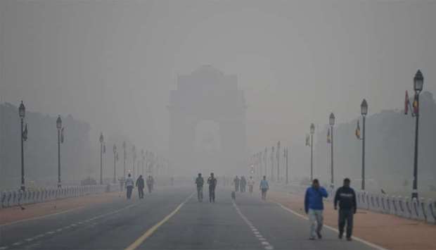 People walk early in the morning as smog covers India Gate war memorial in New Delhi