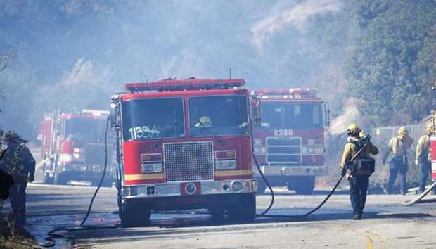 Firefighters work on hoses next to fire trucks as they battle the Woolsey fire in West Hills