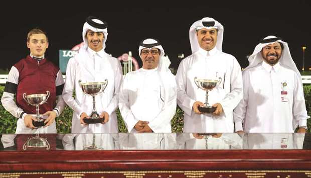 Qatar Racing and Equestrian Club (QREC) Racing manager Abdulla Rashid al-Kubaisi (centre) and Grandstand and Protocol head Saad al-Hajri (right) with the winners of the Umm Al Houl Cup, after Harry Bentley rode Injaaz Studu2019s Izzthatright, trained by Jassim Mohamed Ghazali, tovictory at the Al Rayyan Park yesterday. PICTURES: Juhaim