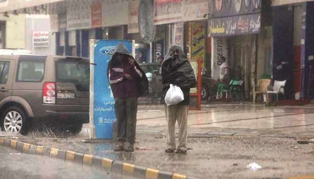 Two young men cover their heads with plastic capes as they stand on the pavement in a commercial district of Kuwait City under heavy rainfall and mist, yesterday.