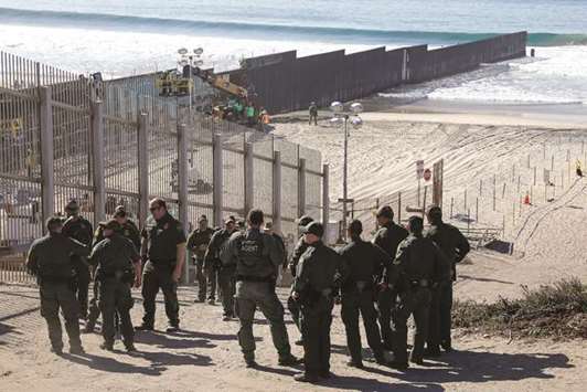 US border patrol agents look over the border fence between Mexico and the United States, where they expect a large group of caravan migrants to gather today, at Border State Park in San Diego.