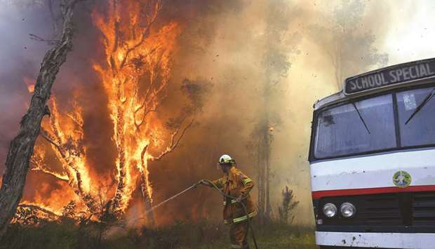 A New South Wales (NSW) Rural Fire Service firefighter sprays water on a bushfire next to a school bus in the suburb known as Salt Ash, located north of Newcastle, in Australia yesterday.