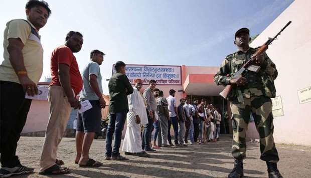 A security official stands guard as voters queue outside a polling station to vote in India's Madhya
