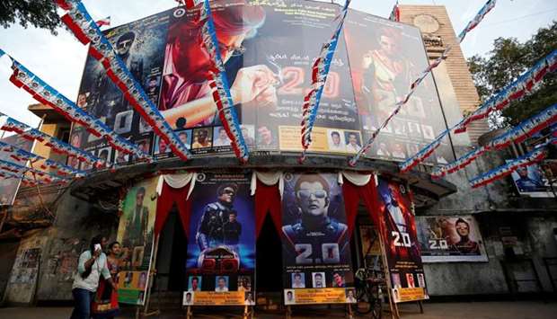Women walk past a cinema decorated with posters of Tamil film star Rajinikanth's new movie ,2.0, on the eve of its release, in Mumbai