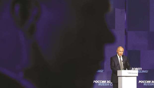 Putin delivers a speech at the VTB Capital Investment Forum, with the silhouette of a security guard seen in the foreground, in Moscow.