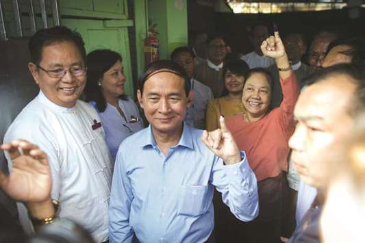 Myanmar President Win Myint, left, followed by his wife Cho Cho displays inked finger after voting at a polling station in Yangon yesterday.