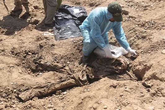 File photo taken on April 12, 2015 shows a member of the Iraqi security forces wearing protective clothes inspecting a mass grave containing the remains of dozens of people believed to have been slain by militants of the Islamic State (IS) group at the Speicher camp in the city of Tikrit.