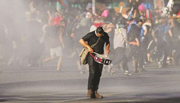 A demonstrator plays the drum as other demonstrators run from a water cannon during an anti-government protest in Santiago early on Wednesday evening.