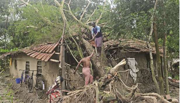 Men cut down an uprooted tree which damaged their house after cyclone Bulbul hit the area in Namkhana, in West Bengal yesterday.