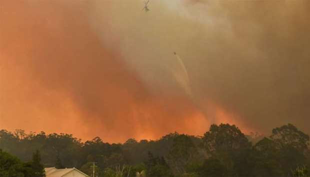 A helicopter drops water on a homestead as bushfires impact on farmland near the small town of Nana Glen, some 600kms north of Sydney