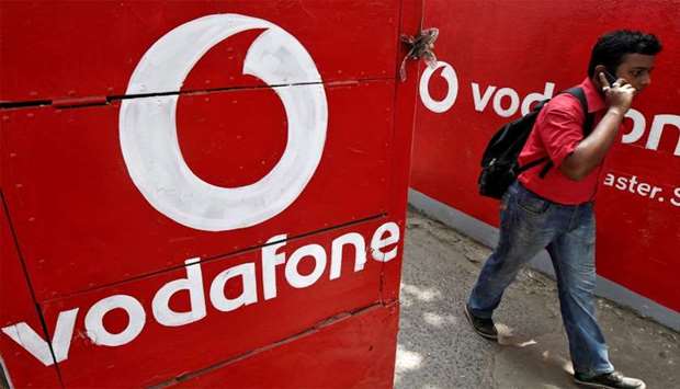 Man speaks on his mobile phone as he walks past the logos of Vodafone painted on a roadside wall in Kolkata