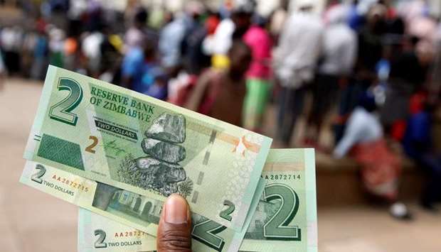 A man poses with Zimbabwe's new two dollar banknotes as customers queue outside a bank in Harare