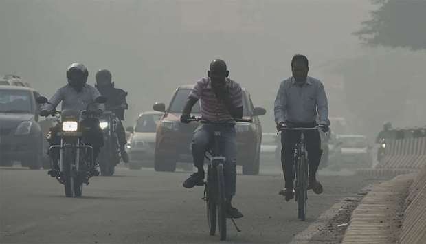 Drivers and cyclists make their way along a road under heavy smog conditions in New Delhi