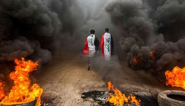 Anti-government protesters draped in Iraqi national flags walk into clouds of smoke from burning tires during a demonstration in the southern city of Basra