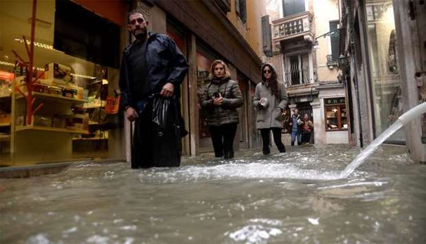 People walks in flooded street as a pump hose spouts water from a shop in Venice, during ,acqua alta,, or high water, of 160 centimetres (over five feet)