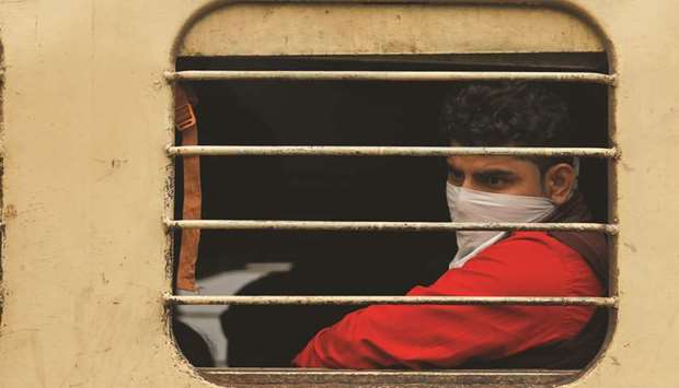 A man with his face covered looks through a window of a train in New Delhi.