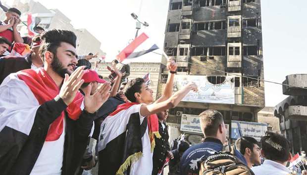 Iraqi protesters march past a burnt-down building near the capital Baghdadu2019s Khallani Square during ongoing anti-government demonstrations, yesterday.