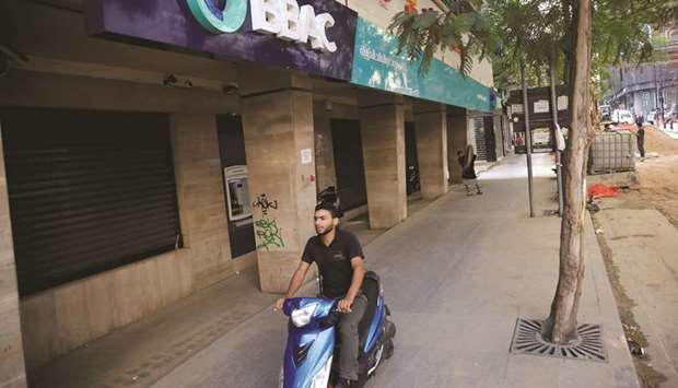 A man drives a motorbike past a closed bank office in Beirut on November 15. Lebanese banks planning to reopen soon will act together for the first time to take emergency measures on the movement of capital amid continuing political turmoil.